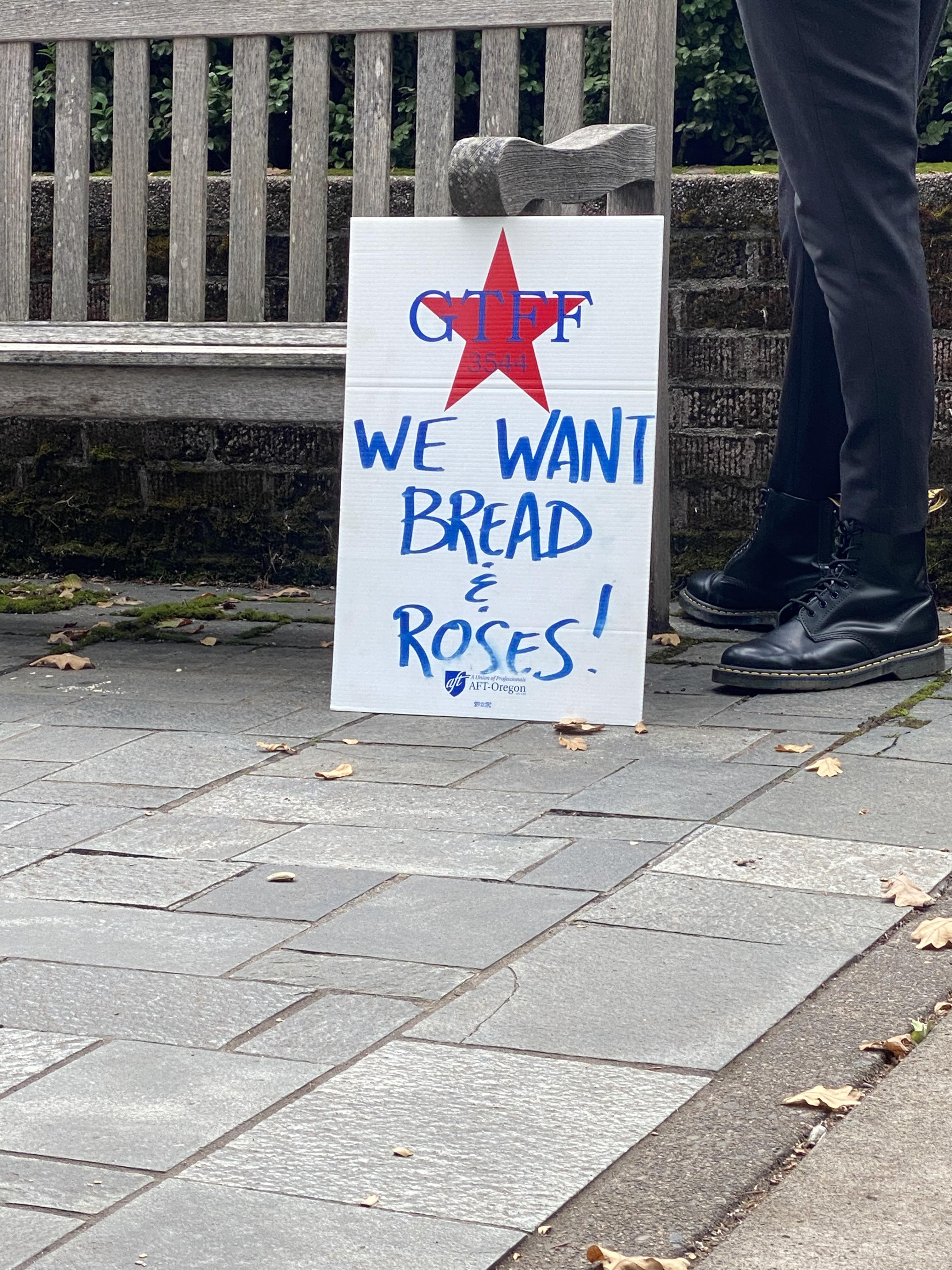 A sign held at the picket reading “We Want Bread & Roses!” Bread and Roses is a political slogan based off of a poem and is commonly associated with the 1912 Textile Strike in Lawrence, Massachusetts - appealing for fair wages and dignified conditions.