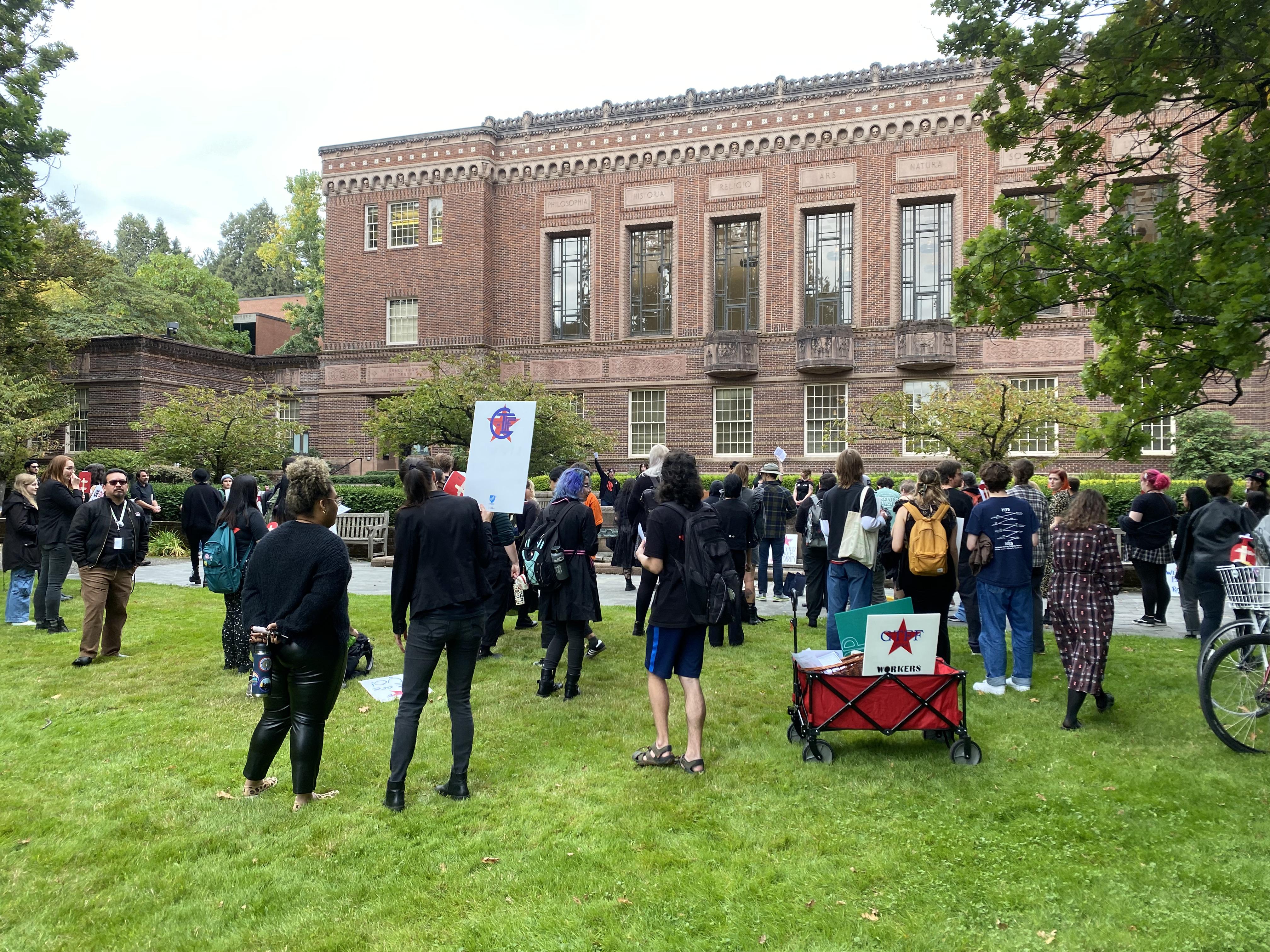 A crowd of protesters, dressed in black, gathered on the lawn outside of the Knight Library. Many people were graduate students / members of GTFF, but there were also a handful of bystanders or supporters that participated.