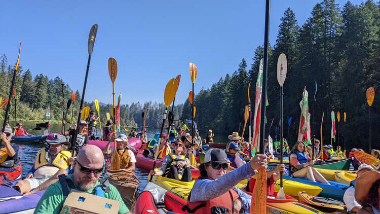 photo of a large number of kayakers with their paddles raised high