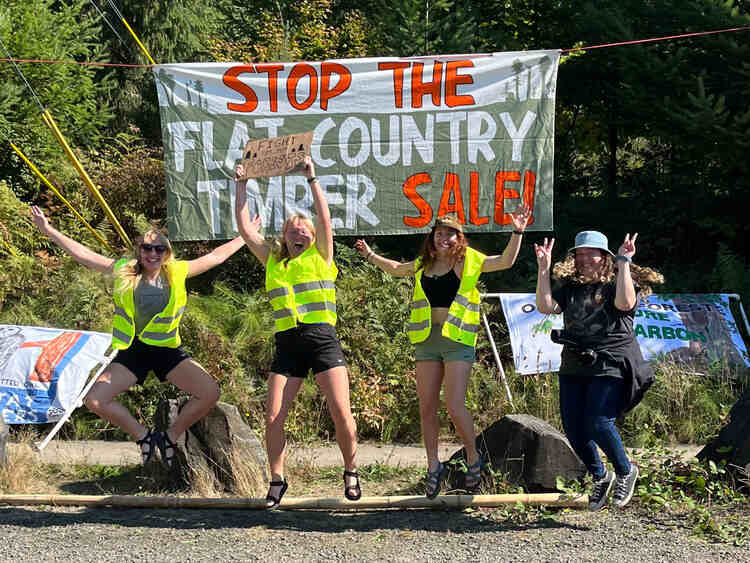 several protestors stand in-front of a banner reading &ldquo;Stop the Flat Country Timber Sale!&rdquo;