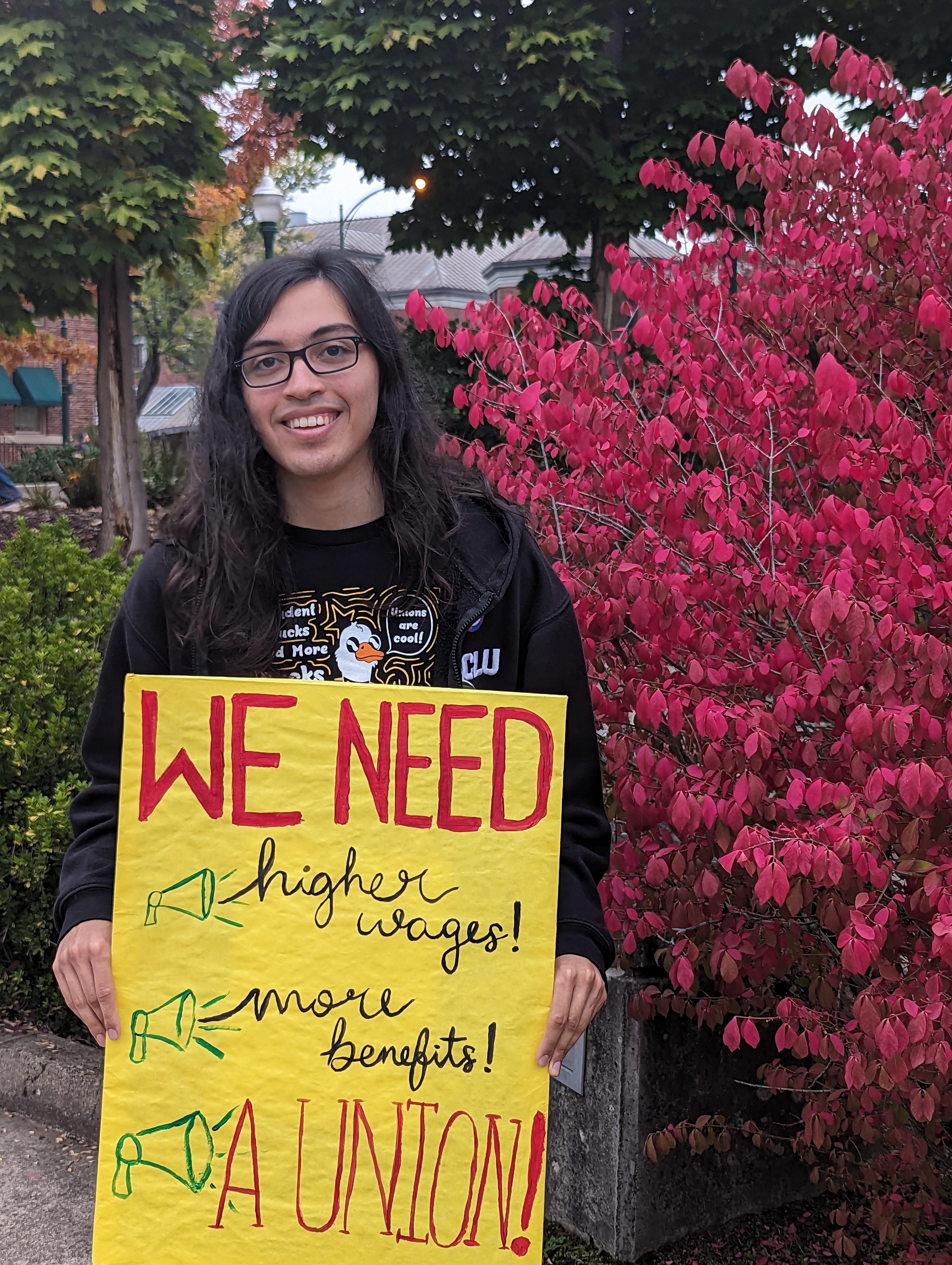 Diego Duarte, UOSW organizer and YDSA political education chair holding a sign &ldquo;We need higher wages! more benefits! A UNION!&rdquo;