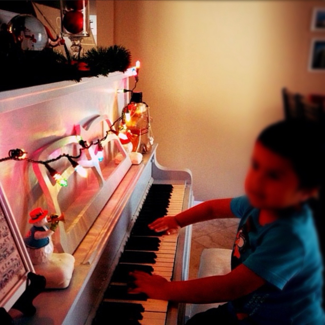 Aesthetically blurry image of a toddler playing the piano underneath the Christmas lights