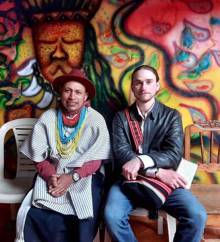 The author sits wiht an Inga shaman in the Sibundoy Valley, southwest Colombia. Colorful art adorns the wall behind them.